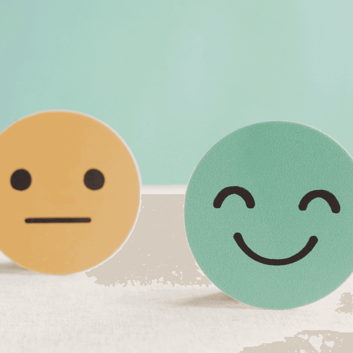 Two emoji faces, one neutral yellow and one happy green, placed against a light background.