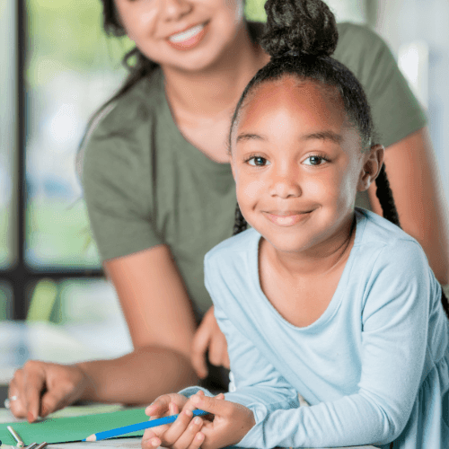 Woman in a green shirt assisting a child with a school assignment at a table.