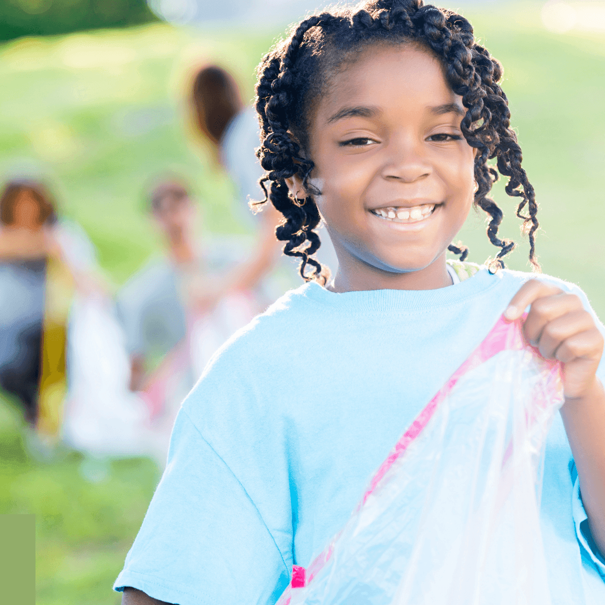 Child holding a plastic bag with other people in the background participating in an outdoor cleanup activity.