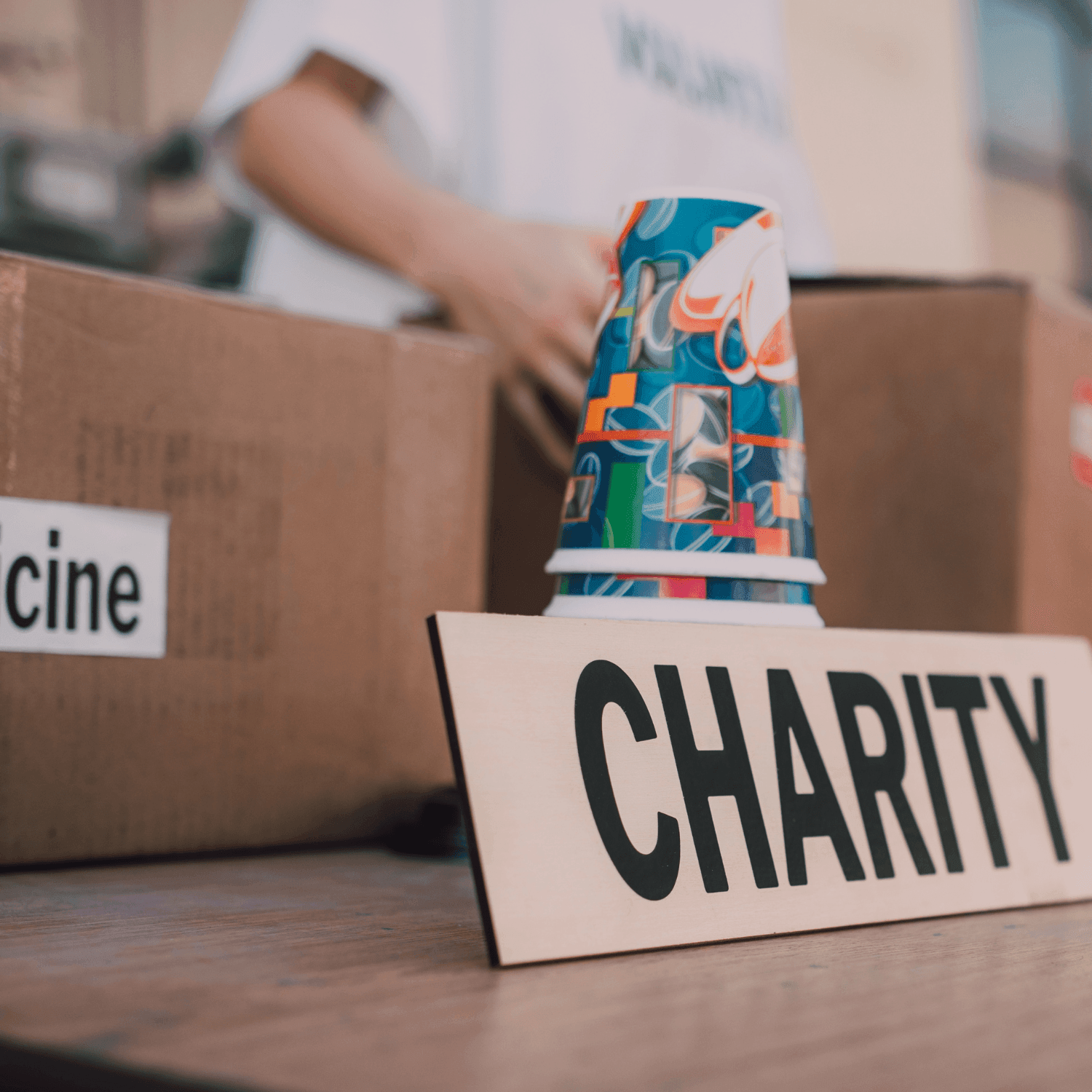 Sign reading 'CHARITY' with colorful cups and cardboard boxes in the background.