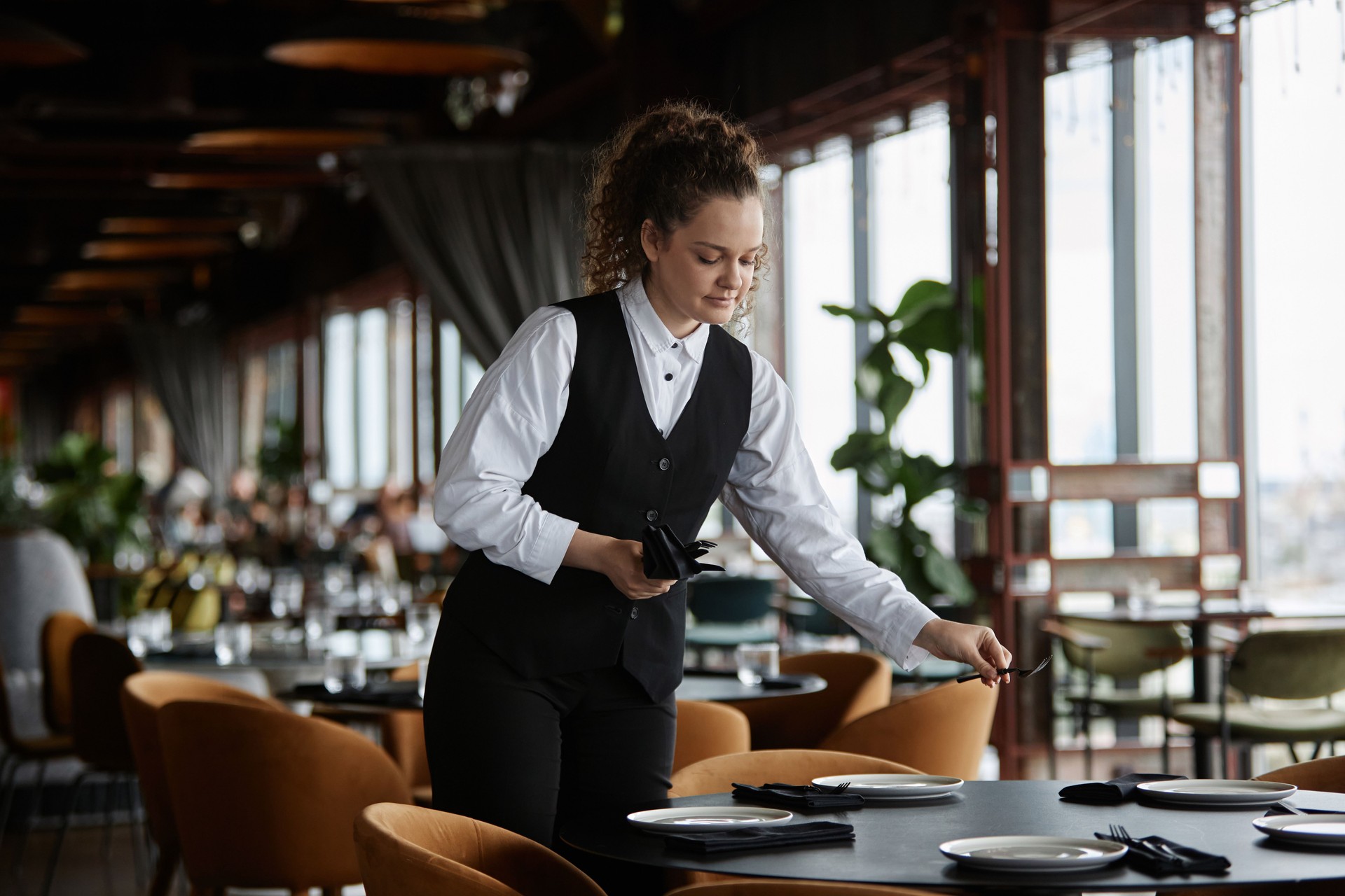 Young woman as female server setting tables in restaurant preparing for opening